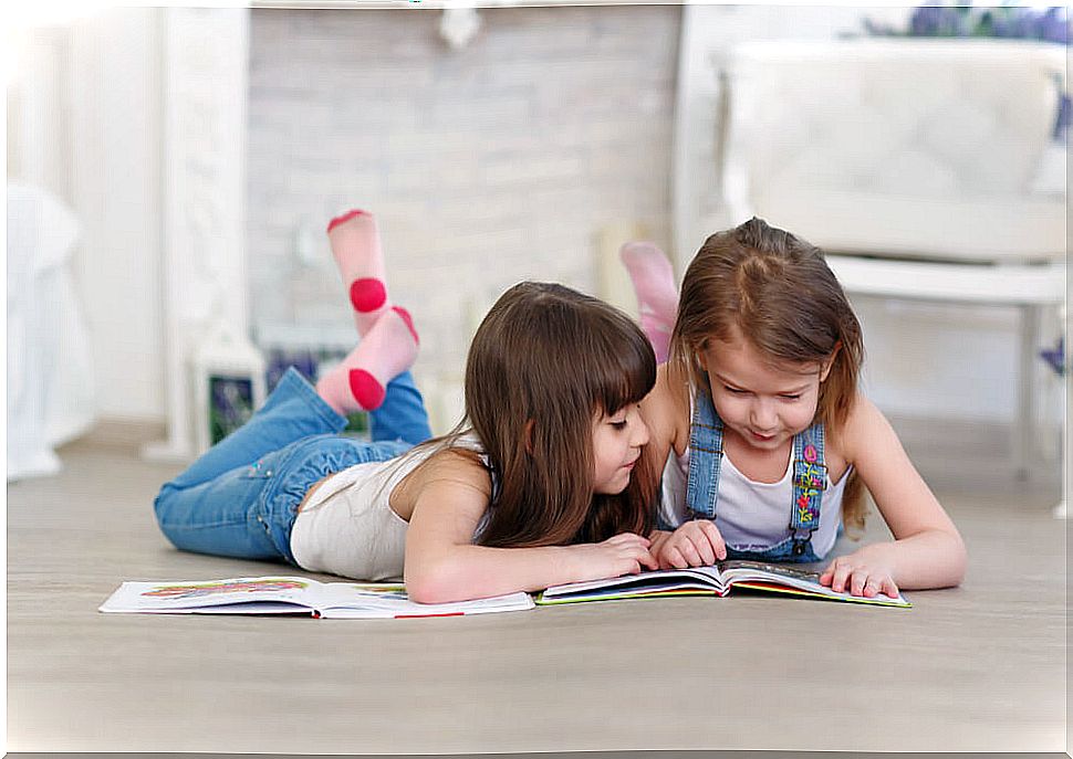 Girls reading children's books lying on the floor to learn letters.