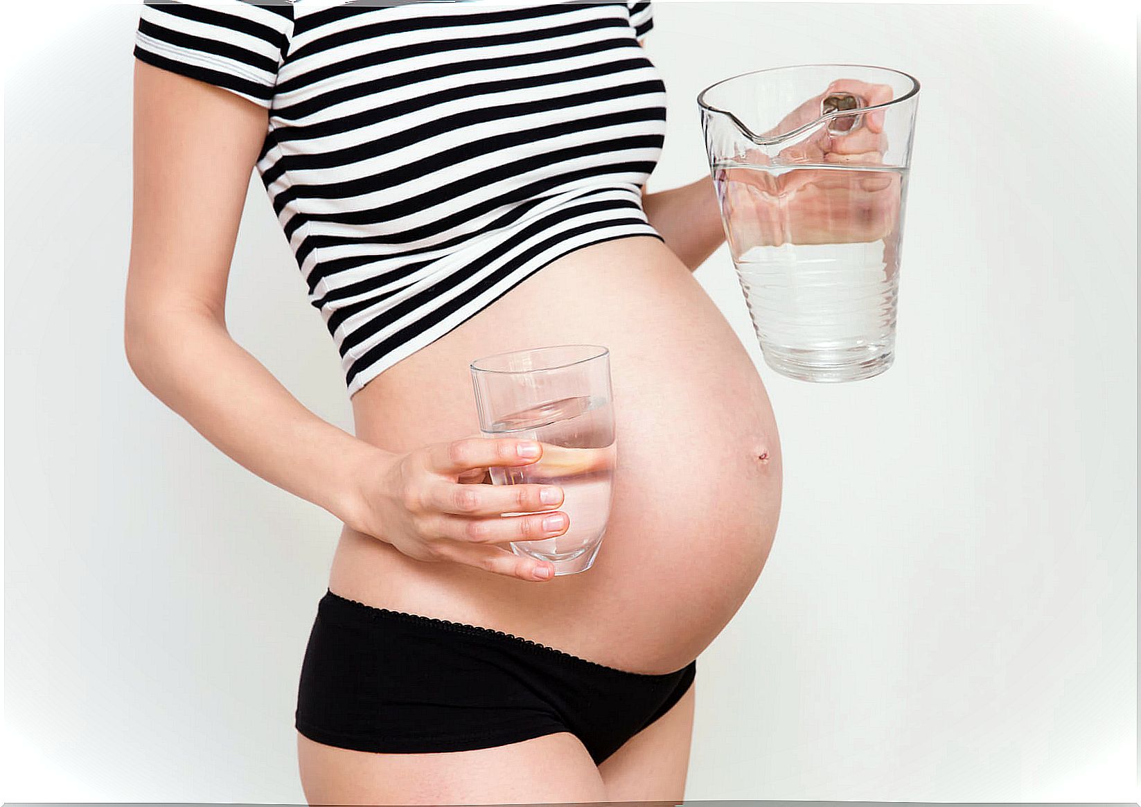 Close up of a cute pregnant belly with a glass of water