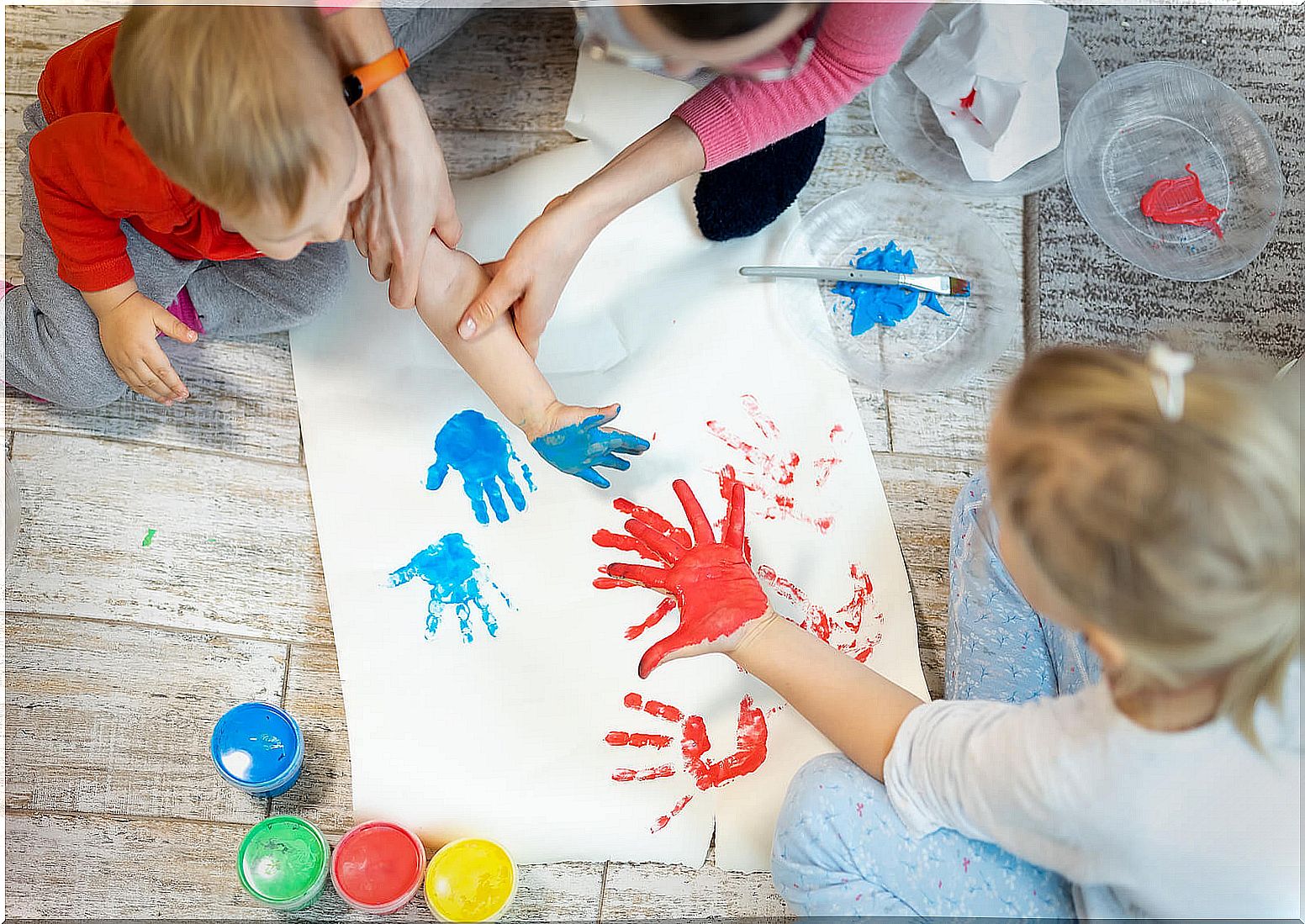 Mother with her children playing finger and hand painting a mural.