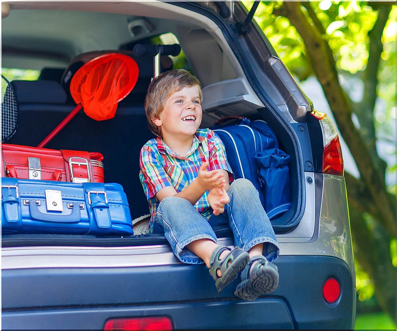 Boy sitting in the trunk of the car before taking a long trip with his parents.