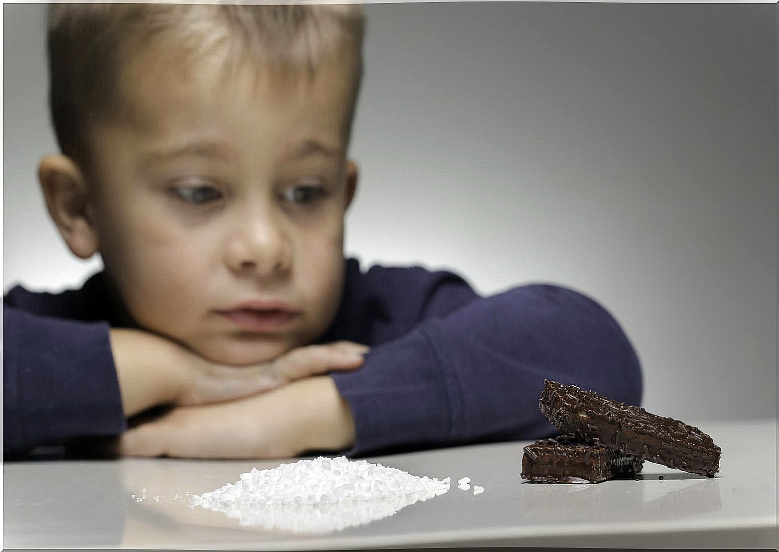 Child looking at a mountain of sugar and a piece of chocolate.