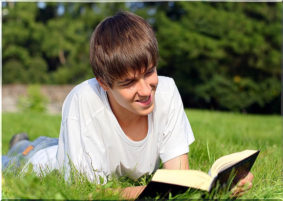 Young boy reading one of the time travel books lying on the grass.