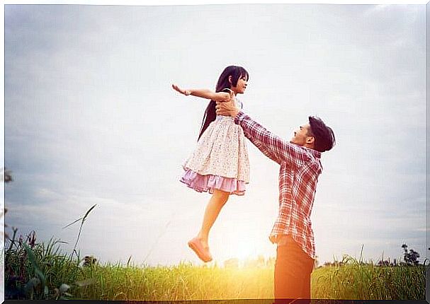 Father lifting his daughter up in the air on the field and practicing positive discipline.